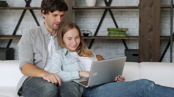 Young Couple Relaxing at Home, Looking at Laptop