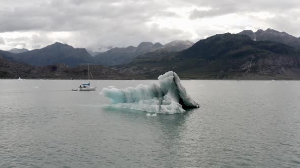 Aerial View of Iceberg and Boat In Cold Water by Alaskan Coastline on Cloudy Day . Global Warming an