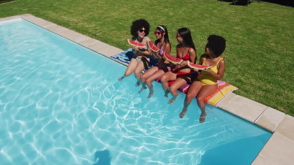 Overhead view of group of diverse girls eating watermelon while sitting by the pool