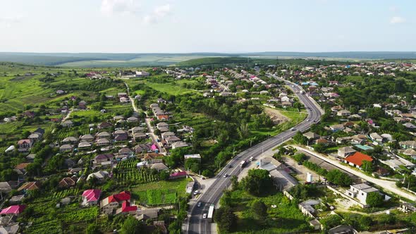 Aerial drone view of a village and road with cars, greenery, hills, Moldova