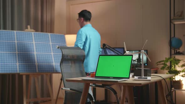 Asian Man Walks Into The Office Looking At Solar Cell That Is Next To The Green Screen Laptop