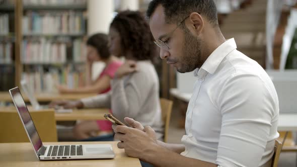 Side View of Focused Young Man Using Smartphone at Library