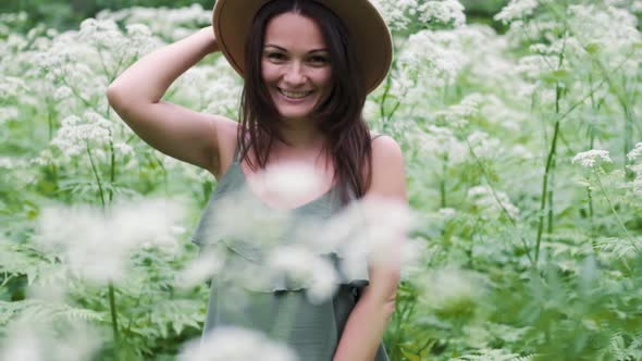 Young Beautiful Woman Posing in a Forest with a Hat on a Background of White Flowers. Happy Brunette