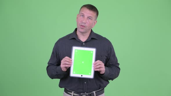 Macho Mature Businessman Talking While Showing Digital Tablet