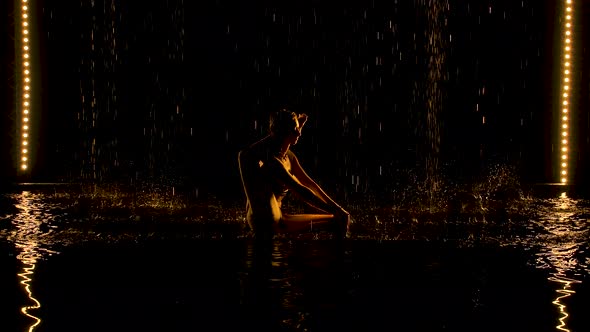 Exercise the Leg Behind the Head. Young Woman Practices Yoga Asanas in a Dark Studio in the Rain