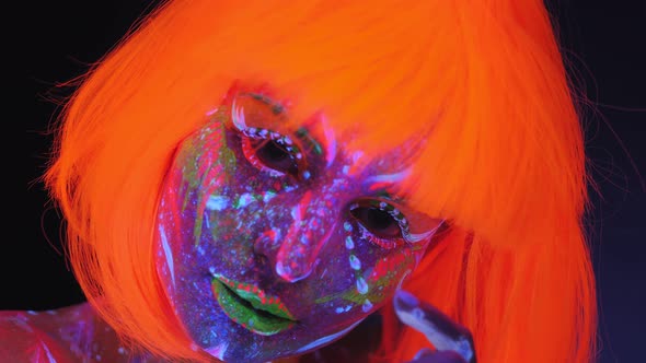 Woman with Glowing UV Drawings on Her Body and an Orange Wig in the Dark