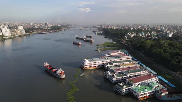 Cargo ship and launches at a river port with city view, aerial drone flying forward shot