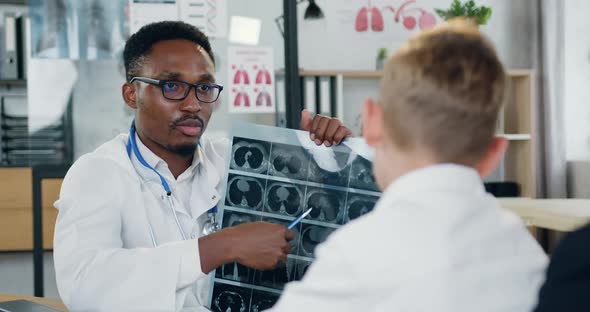 Doctor in White Gawn Explaining Diagnisis of His Teen Boy with Caring Mother Using Boy's X-ray Scan