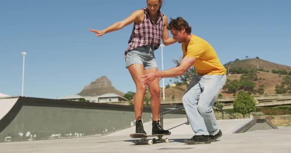 Smiling caucasian man teaching woman how to skateboard on sunny day