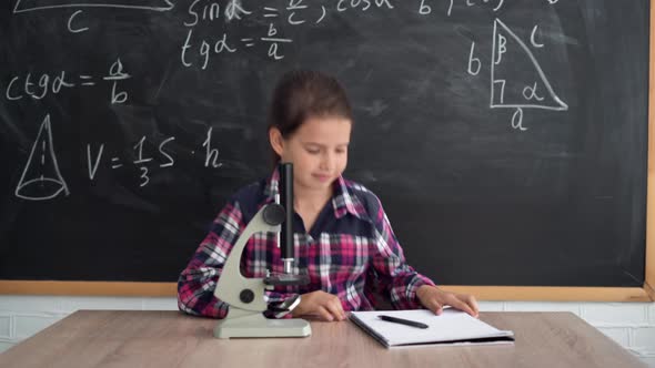 A Little Girl Schoolgirl in a Shirt Stands Against the Background of a Chalk Board