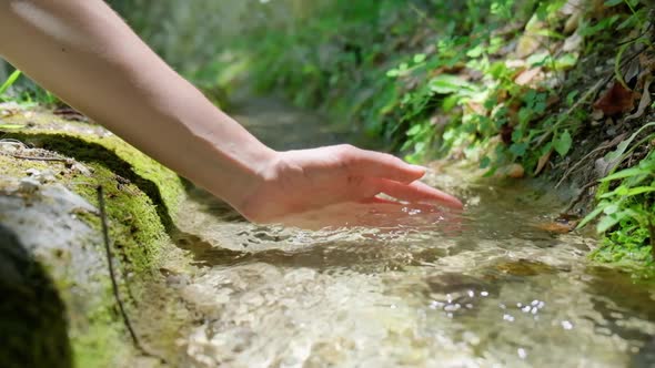 Hand touching flowing stream water.