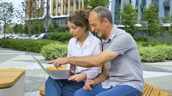 Attractive Young Woman and Senior Man are Using Laptop Sitting on the Bench in Modern Residential