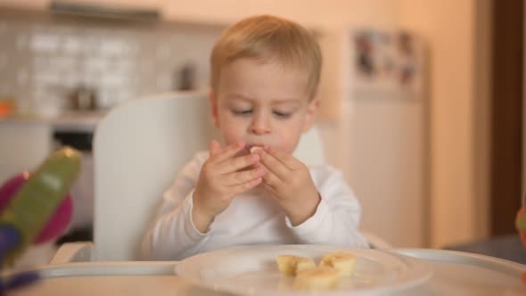 Little Happy Cute Baby Toddler Boy Blonde Sitting on Baby Chair Playing with Banana