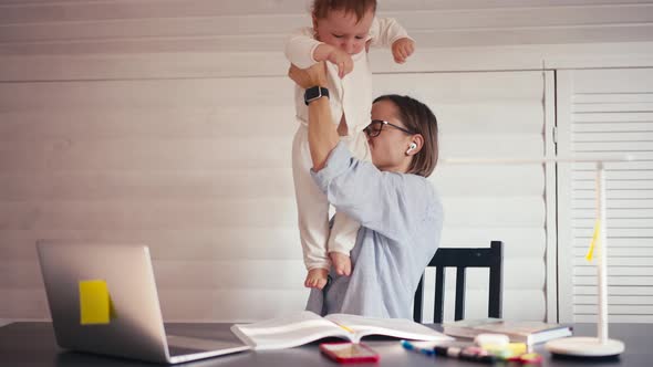 A Young Mother is Working at Home Using Computer While She's Taking Care of Her Baby