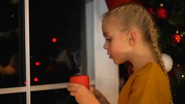 Girl Blowing on Candle Standing Near Window Waiting Parents