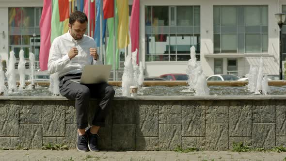 Man with Laptop Sitting Near Fountain and Happy with the Results of His Work