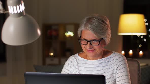 Happy Senior Woman with Laptop at Home in Evening