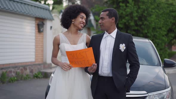 Happy African American Young Couple Standing at Car Holding Just Married Sign Talking Smiling