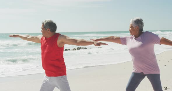 Happy and relaxed hispanic senior couple practicing yoga on beach
