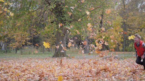 Boy Runs Through a Cloud of Floating Autumn Yellow Leaves.