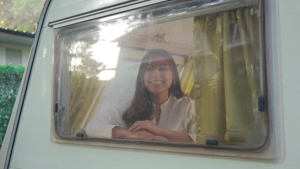 cheerful young woman waiving saying hello at window of a camper RV van motorhome