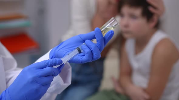 Closeup Doctor Hands Filling Syringe with Injection As Blurred Scared Caucasian Boy Sitting at