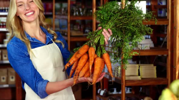 Smiling staff holding bunch of carrots in organic section