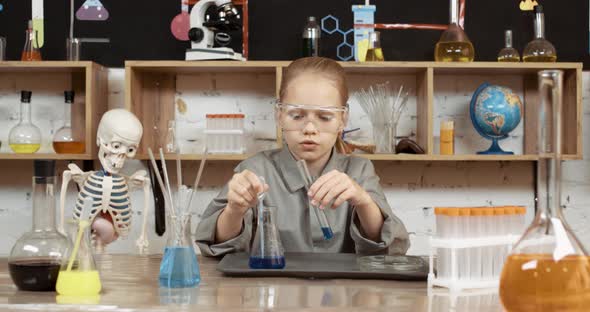 Laboratory Experience in a Chemistry Lesson, a Girl in Protective Glasses Pours a Blue Liquid Into a