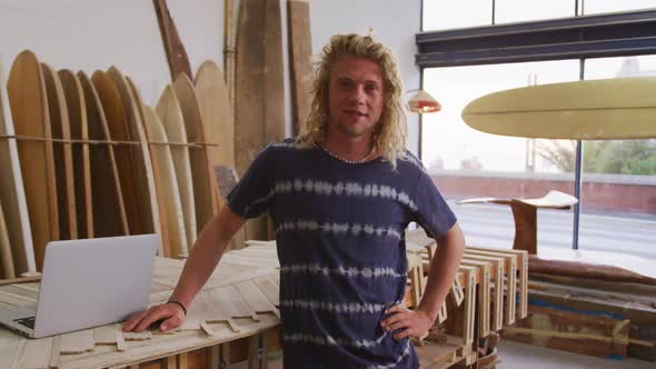 Caucasian male surfboard maker in his studio with surfboards in background