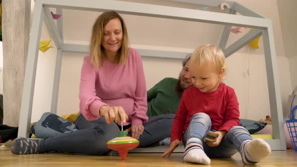 Father and mother showing spinning toy to Infant son at children room. alt