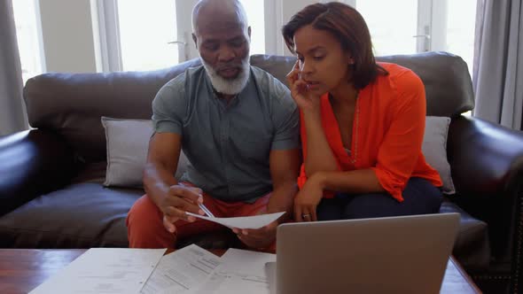 Front view of mature black couple sitting on the couch and discussing bills in a comfortable home 4k