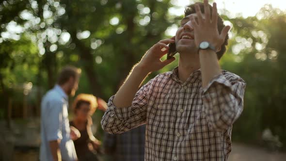 Young Handsome Caucasian Male Joyfully Talking on Mobile Phone Smiling Laughing While Groupe of