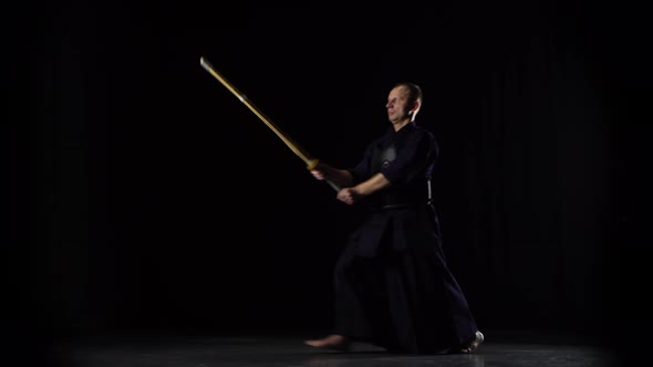 Masculine Kendo Warrior Practicing Martial Art with the Bamboo Bokken on Black Background.