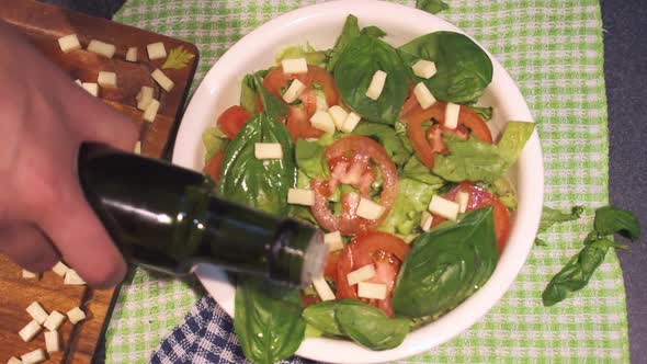 Hands making a lettuce and tomato with basil, adding olive oil in a white bowl