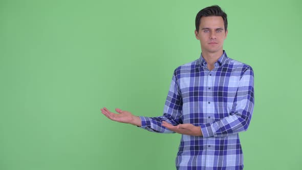 Happy Young Handsome Hipster Man Showing Something and Giving Thumbs Up