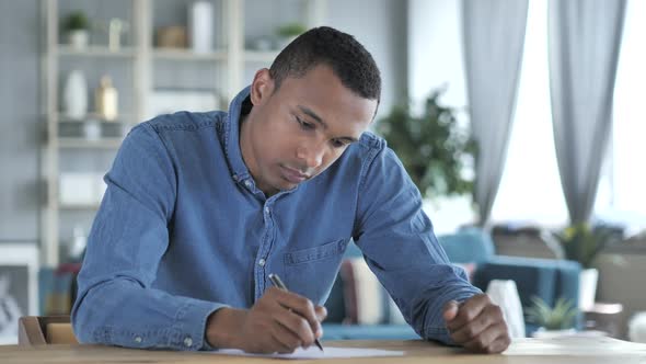 Young African Man Writing on Documents in Office Paperwork