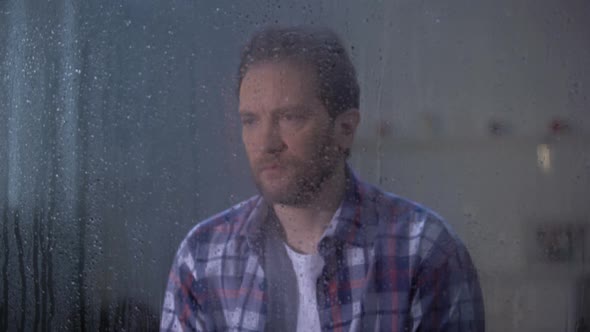 Lonely Man Sitting Behind Rainy Window and Looking at Camera Depression