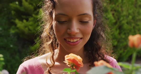 Portrait of happy biracial woman smelling roses in garden