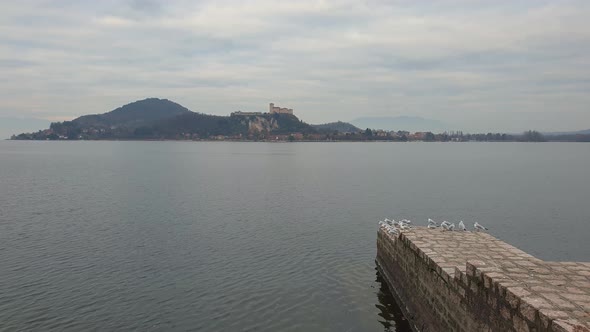 Flock of seagulls on pier boardwalk on Maggiore lake with Angera fortress in background