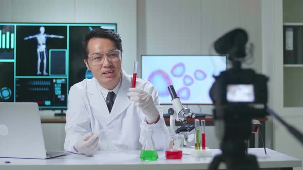 Asian Scientist Researching In The Laboratory With Test-Tube And Speaking To The Camera