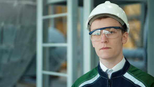 Young Engineer Wearing Protective Helmet Posing Looking at Camera at Modern Factory