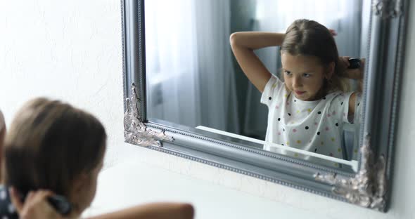 Pretty Little girl combing by herself hair in front of a mirror