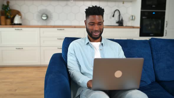 Cheerful Man Wearing Casual Clothes Sitting on the Sofa and Using Laptop at Home