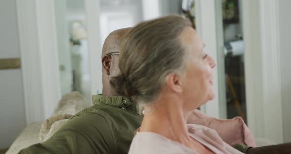 Happy senior diverse couple wearing shirts and watching tv in living room