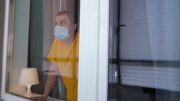 COVID-19 Pandemic Coronavirus. Quarantine Man in Medical Mask on Face Looking Through the Window