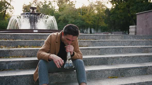 Handsome Stylish Young Man Sitting on Stairs and Smoking Weed with Bong in Park Slow Motion