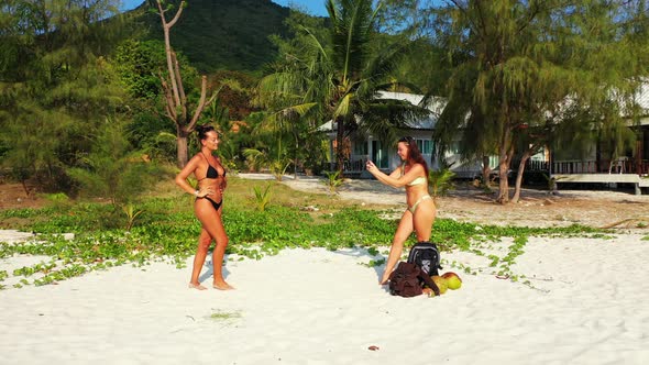 Young smiling girls on photoshoot in the sun at the beach on paradise white sand and blue background