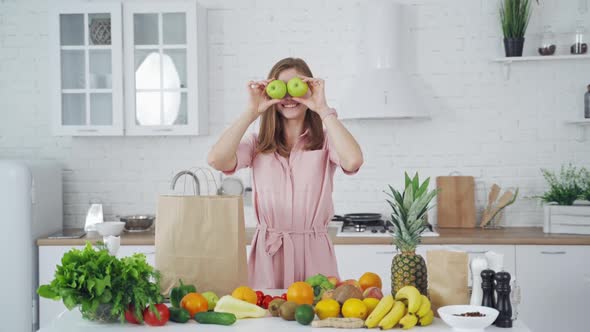 Funny young woman closes her eyes with two green apples indoors.