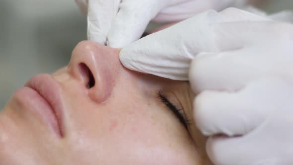 Doctor Beautician in a Black Mask Makes Cleaning the Face of a Young Woman