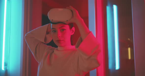 Young woman holding vr goggles in hand in red neon light looking into the camera